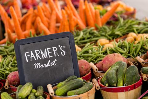 A chalkboard, "Farmer's Market", surrounds with baskets of vegetables.