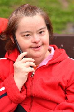 Person with Down syndrome wearing a red jacket talking on a cell phone