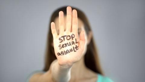 Adult woman with hand in front of face with Stop Sexual Assault written on it.