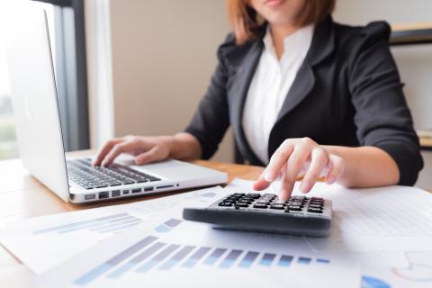 An adult using a computer and calculator same time