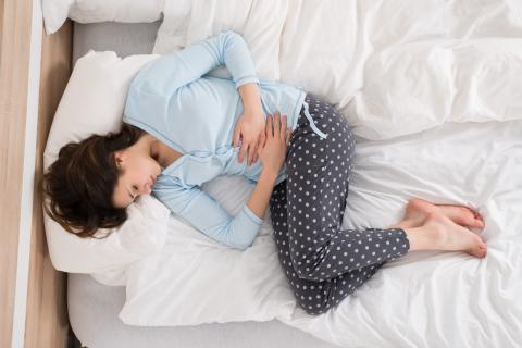 A person curled up on its side on a bed with hands on stomach