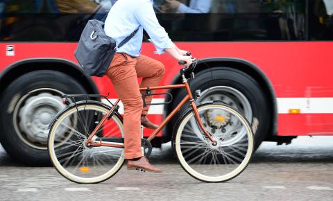 An adult with a briefcase riding bicycle next to a bus.