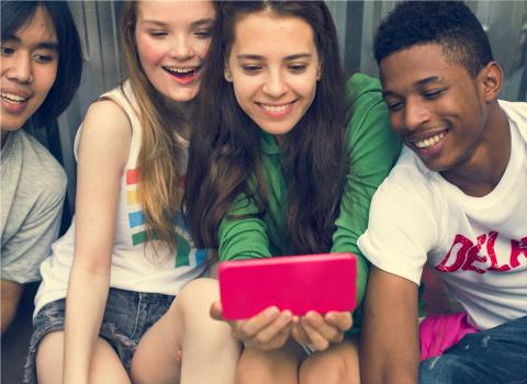 Four teens watching a cell phone