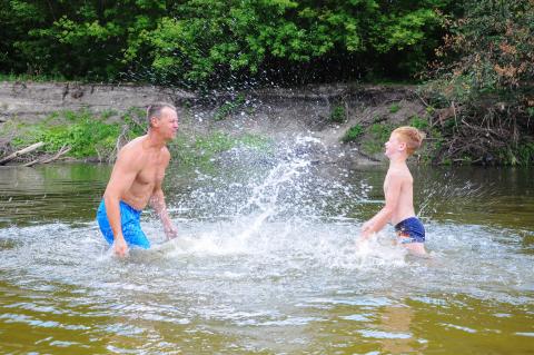 An adult and a child splashing water in a river.