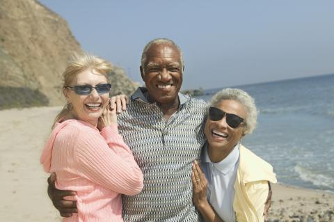 Three smiling adults hugged by a beach.