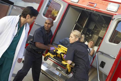 Two EMTs delivering a patient to hospital with a doctor in white coat looking on