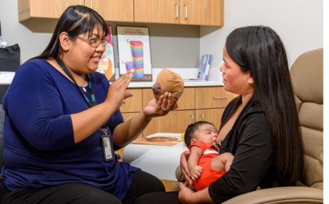 WIC peer counselor gives advice to a WIC participant while the participants breastfeeds an infant.