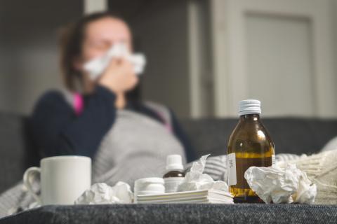 Ill adult blowing nose with used tissues and meds on table.