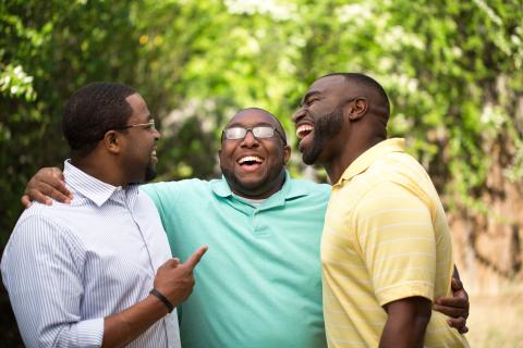 Three adults hugging and laughing outside.
