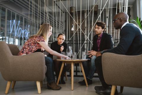 A workgroup of four adults in progress around a table with word "work" on a wall