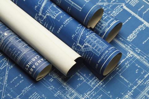 Four rolls of blue blueprints with one white one on opened blueprint.
