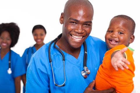 A smiling doctor holds a smiling child.