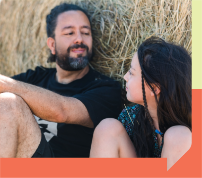 An older person and a younger person sitting by a hay bale