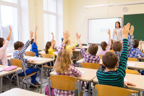 Students in a classroom raising their hands to answer a question