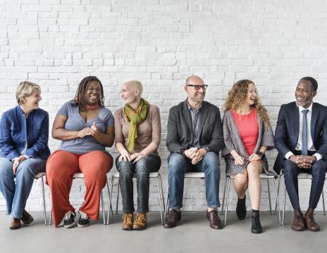 Six adults sitting in chairs against the wall