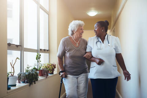 A caregiver assisting an older adult to walk down a hallway