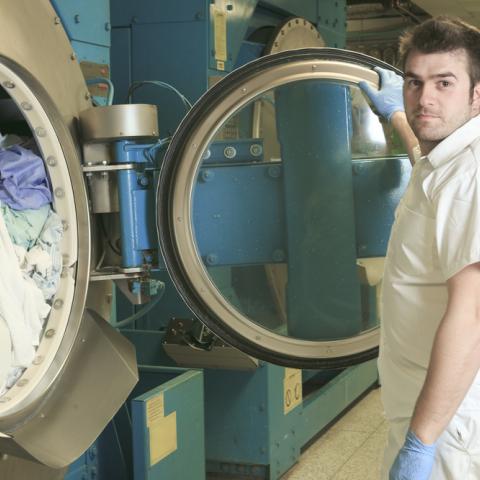 Laundry attendant attends to a commercial washing machine