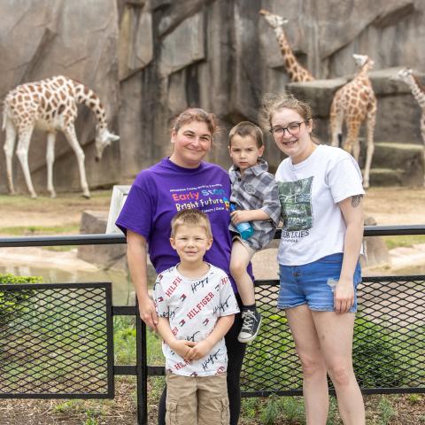 Milwaukee County Birth to 3 ARPA Grant: Smiling Birth to 3 family at zoo with giraffes in background