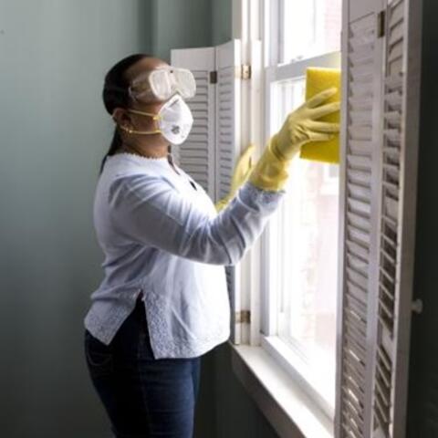 Adult wearing goggles, yellow gloves and a mask cleaning the window.