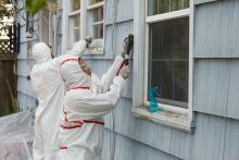 Two adults in hazmat suits removing lead paint from a building.