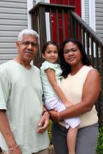 A family of three standing front of a house.