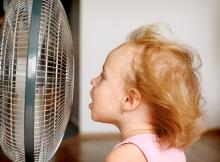 A toddler standing front of a running fan.