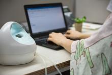 An adult on a laptop with a breast pump on the desk