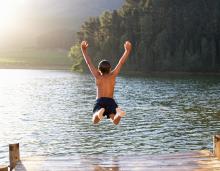 Young child jumping into lake from a pier with arms up