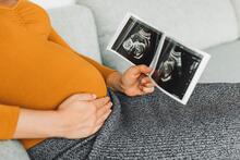 Pregnant person with hand on belly holding an ultra sound picture