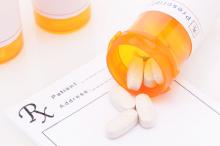 An opened bottle of prescription pills on top of prescription pad.