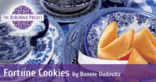 Three fortune cookies sitting in a blue and white floral bowl on a table with other matching china. Image is overlaid with The Remember Project logo and banner that reads "Fortune Cookies by Bonnie Dudovitz"