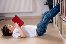 A child lying on the floor reading a book with his feet up on a bookcase