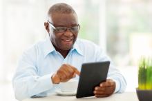 Smiling man uses a tablet with a coffee cup