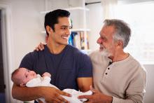 An adult holding a baby with and older adult's arm on their shoulder