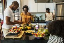 Two adults and two children prepare a meal together at home.