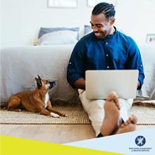 Adult on laptop in bedroom with dog sitting at their side