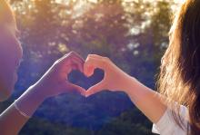 Two adults forms a heart shape with their hands.