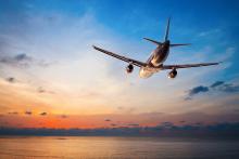 An airplane flies above the sea at sunset