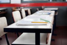 Empty classroom, a desk and notebooks with a red bar across on the top