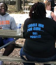 Young adults at picnic table, adult with back to camera has t-shirt stating: Labels are for cans...not people!