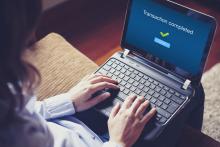 Laptop with transaction completed on the screen, hands over the keyboard on a person's lap