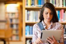 A young adult looking at her tablet in a library