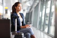 An adult waits at an airport with a suitcase.