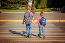 Two children wearing backpacks and holding hands crossing the street at a crosswalk