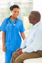 A medical technician talks to an adult sitting on an examination table at the clinic