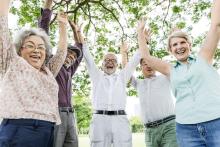 Five smiling older adults with their arms up outdoors