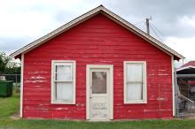 Side of red shed type building with peeling paint and door.