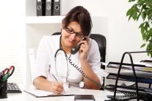 Doctor taking notes at desk while on the phone.