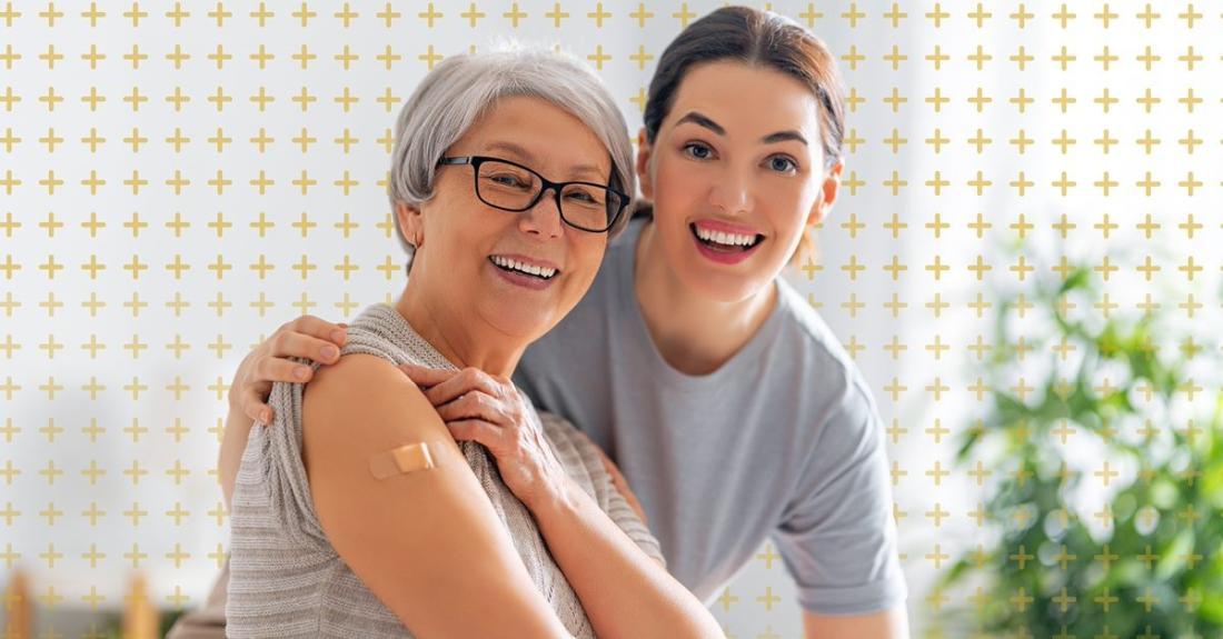 A younger adult with arm around an older adult who is showing vaccinated arm